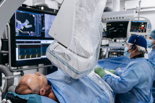 Cardiologist performing a catheter procedure on a patient using fluoroscopy and medical monitors inside a modern hospital cath lab.