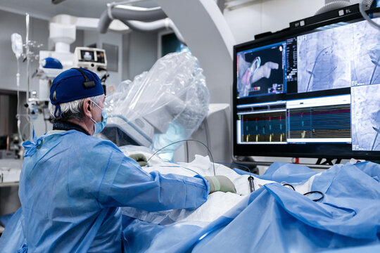 Cardiologist operating a catheter while monitoring fluoroscopy images and cardiac signals on a large medical screen during a heart procedure.