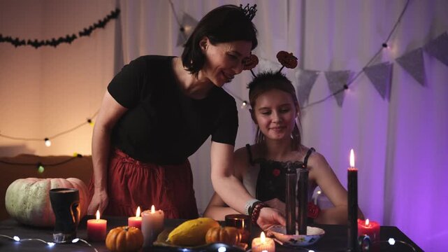 Mother And Daughter Celebrating Halloween In A Decorated Room, Blowing Out A Burning Candle Flame