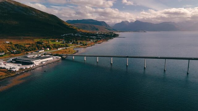 Smooth 180 degree drone pan over a scenic bridge crossing a wide body of water with traffic under a dramatic cloudy sky in Norway
