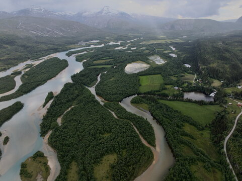 Aerial view of a braided river with river islands, lush green vegetation, and snow-capped mountains in the background in Skonseng, Nordland, Norway.