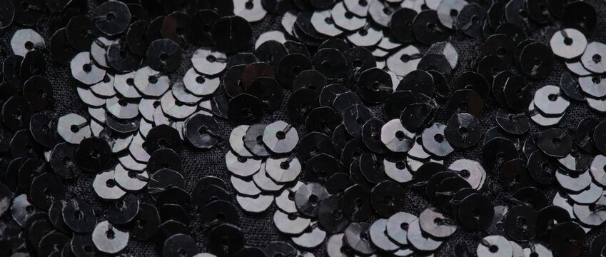 Close-up of overlapping black sequins on fabric. Dark shiny reflective texture background. Glamorous festive party material
