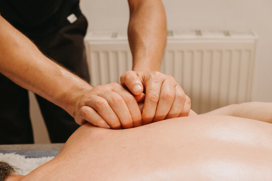 therapist hands applying deep tissue kneading to adult clients bare back with oil and gentle light in clinic.