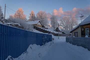 Quiet street with private village houses in the Far North of Russia covered in snow at pink sunset. © PuzzleSoul
