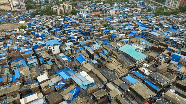 Aerial view of the dense urban landscape of Dharavi Slums with characteristic blue tarpaulin roofs and narrow alleyways in Mumbai, Maharashtra, India.