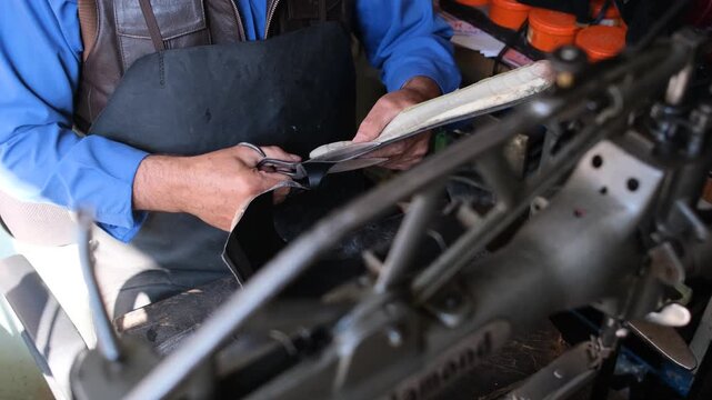 Manisa, Turkiye - 19 June 2026: View of a skilled shoemaker cutting black leather with scissors in a traditional workshop with a sewing machine.