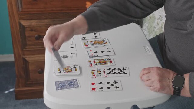 Gordonville, United States - 20 March 2026: View of a person playing a card game on a white table with various playing cards laid out.