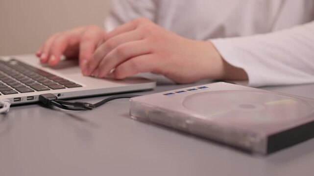 Hands carefully insert disc into drive. Closeup of disc being placed in external drive. Closeup shot showing precise placement of DVD into external USB drive with soft lighting