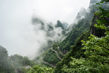 Obraz premium A dramatic bird's-eye perspective of the famous winding serpentine road cutting through the steep, mist-covered karst mountains of Tianmen Mountain National Park in China.