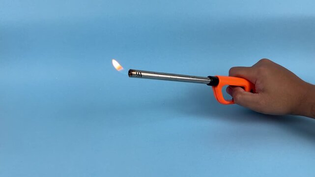 Hand Holding Long Gas Lighter with Flame on Blue Background