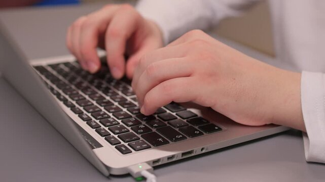 Coding hands work. Person in white sleeve entering commands on silver device. Detailed shot of hands typing code on modern laptop illuminated by soft studio lighting