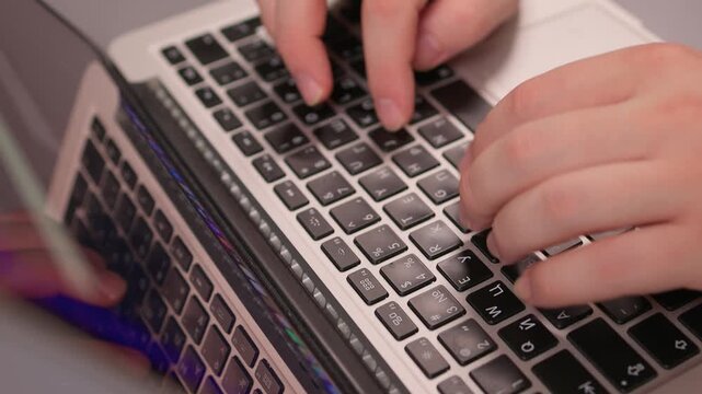 Coding hands work. Person in white sleeve entering commands on silver device. Detailed shot of hands typing code on modern laptop illuminated by soft studio lighting