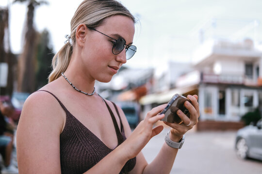 Young female traveler using smartphone outdoors, mobile travel planning, navigation and online booking during solo summer trip, modern connected travel lifestyle.