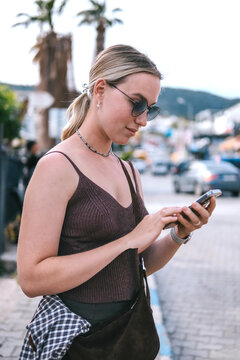 Young female traveler using smartphone outdoors, mobile travel planning, navigation and online booking during solo summer trip, modern connected travel lifestyle.