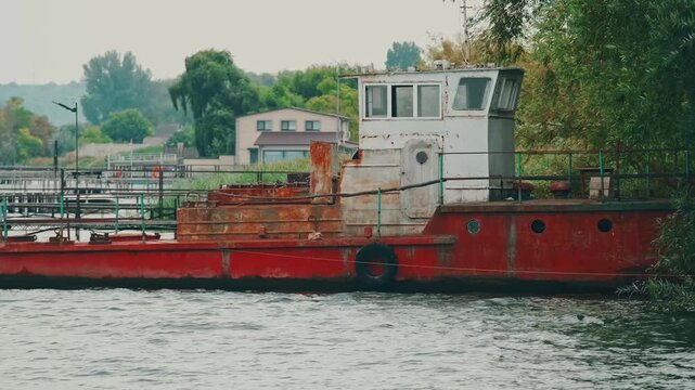 weathered workboat hull shows rust streaks. ropes and fenders rest by willows as gray river ripples quiet too