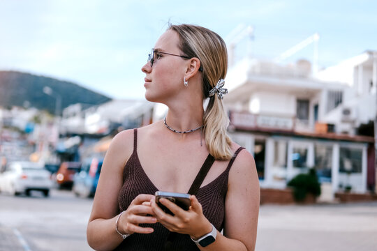 Young female traveler using smartphone outdoors, mobile travel planning, navigation and online booking during solo summer trip, modern connected travel lifestyle.