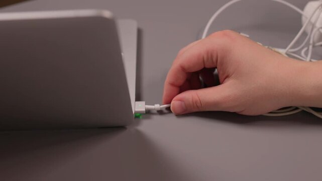 Laptop power cord repair process. Careful examination of frayed laptop connector wires. Closeup view of technician inspecting compromised power cable connections on desk
