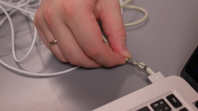 Laptop power cord repair process. Careful examination of frayed laptop connector wires. Closeup view of technician inspecting compromised power cable connections on desk