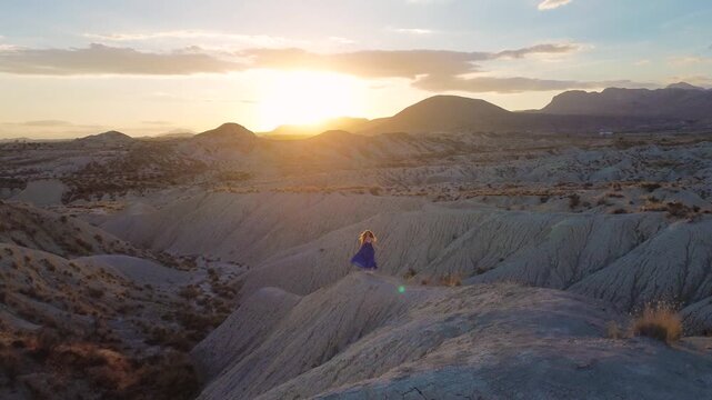 Cinematic Aerial View of Woman in Blue Dress Walking Through Desert Badlands at Sunset in Murcia Spain