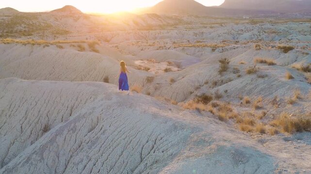 Cinematic Aerial View of Woman in Blue Dress Walking Through Desert Badlands at Sunset in Murcia Spain