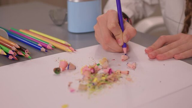 Detailed shot of hands spreading bright pencil shavings on paper. Intimate scene capturing hands organizing colorful debris for artistic collage in soft lighting