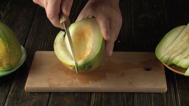 Hands slice green melon on wooden cutting board, removing rind and preparing fresh fruit pieces in a rustic kitchen setting from overhead view