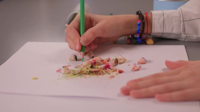Detailed shot of hands spreading bright pencil shavings on paper. Intimate scene capturing hands organizing colorful debris for artistic collage in soft lighting