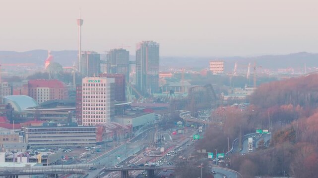 Gothenburg, Vastra Gotaland Count, Sweden - 19 January 2026: View of the city skyline with modern buildings, traffic on the highway, and surrounding hills during sunset.