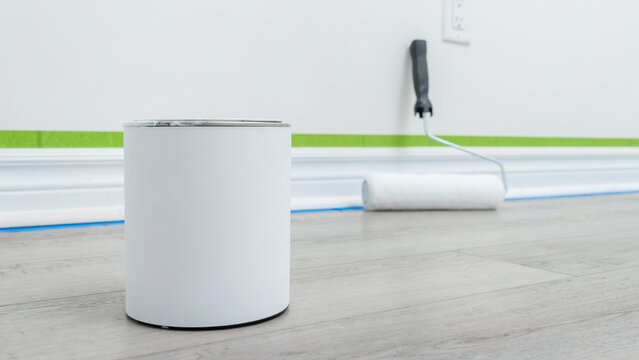 Home renovation mockup featuring a paint can and roller on a wooden floor with green painter's tape along the wall