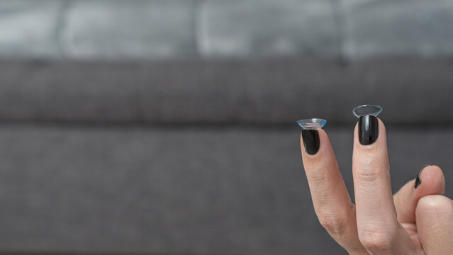 Teenager holding one-day contact lenses in each hand, with a blurred gray couch in the background, showcasing clear lens details and manicured nails