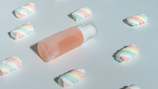 Mockup of a transparent cosmetic bottle with pink liquid surrounded by pastel-colored marshmallow candies on a light background