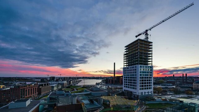 Helsinki, Uusimaa, Finland - 29 October 2022: View of the Kalasatama high rise construction site featuring a tall building under development with a crane against a vibrant sunset sky. Timelapse.
