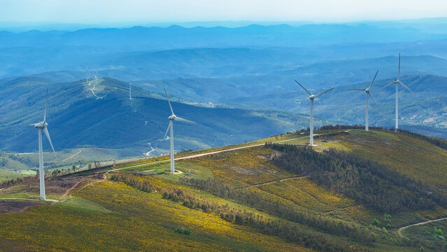Aerial view of wind turbines situated on rolling hills covered with yellow wildflowers and green vegetation under a clear blue sky in Lisbon, Lisbon, Portugal.