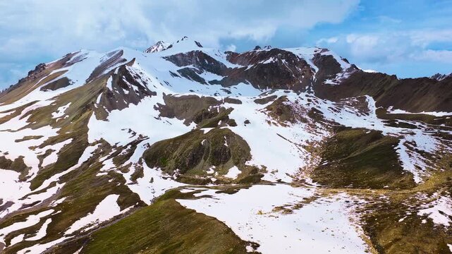 Majestic snow-capped mountain peaks rise sharply beneath a partly cloudy sky, showcasing rugged alpine terrain during a clear day.