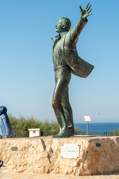 Polignano a Mare, Italy - Aug 3, 2026: Bronze statue of singer Domenico Modugno with arms outstretched standing on a stone base on the seafront with the Adriatic Sea behind
