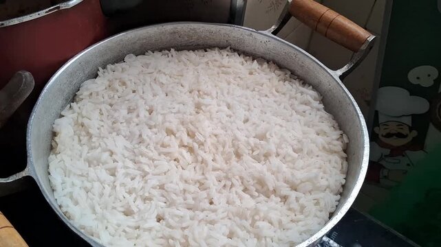 Freshly cooked white rice steaming inside large metal kitchen pot
