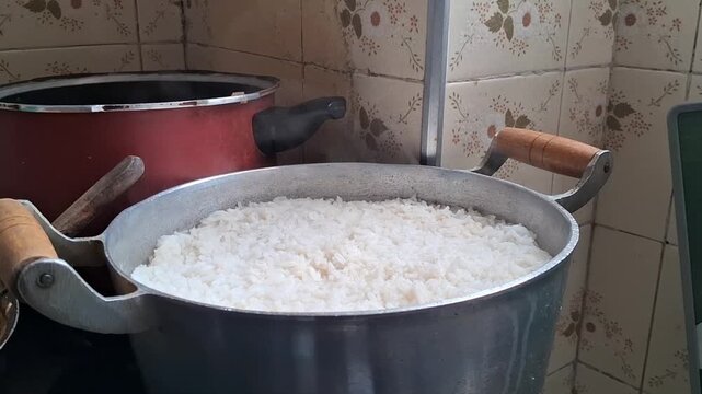 Freshly cooked white rice steaming inside large metal kitchen pot