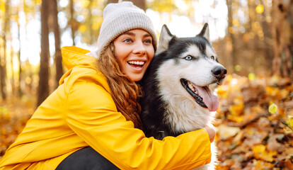 Young woman in yellow raincoat walks with husky through an autumn forest. Woman enjoys moment with pet, surrounded by yellow leaves at sunset. A concept of friendship and walking. © maxbelchenko