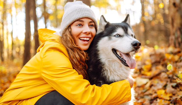 Young woman in yellow raincoat walks with husky through an autumn forest. Woman enjoys moment with pet, surrounded by yellow leaves at sunset. A concept of friendship and walking.