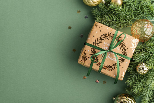 Christmas present wrapped in festive paper with green ribbon surrounded by pine branches and baubles