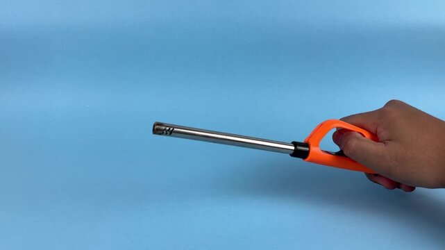 Hand Holding Long Gas Lighter with Flame on Blue Background