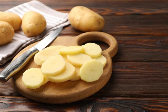 Fresh raw potatoes and knife on wooden table, closeup. Space for text
