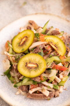 Meat salad with beef, kiwi and vegetables on brown concrete, side view, close up, selective focus