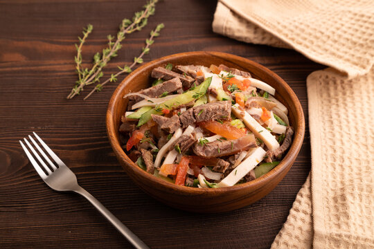 Meat salad with beef and vegetables on brown wooden, side view, close up