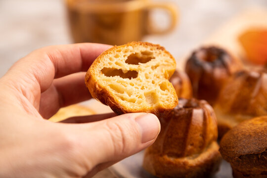 Golden caramelized Canele with hand on brown concrete, selective focus, side view