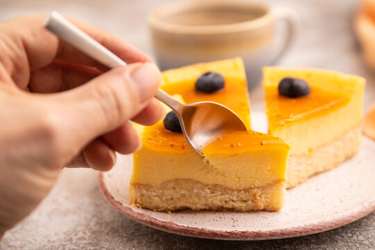 Cheesecake with mango cream with hand on brown concrete, selective focus, side view