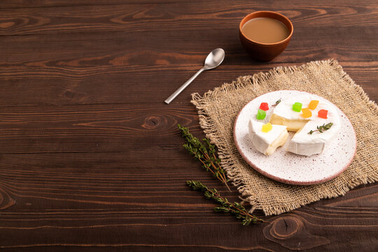 White Camembert mold cheese on brown wooden background and linen textile, cup of coffee, side view