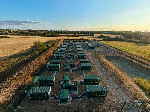 Aerial view of the Battery Energy Storage System at BESS Grendon with rows of green battery containers on a gravel site surrounded by agricultural fields in Northampton, England, United Kingdom.