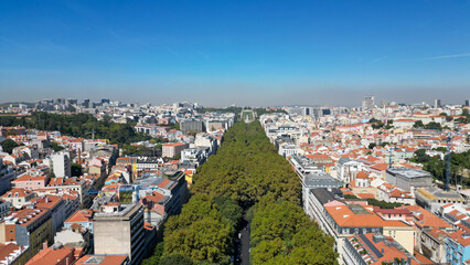 Obraz premium Aerial view of Avenida da Liberdade in Lisbon, Portugal, featuring the iconic tree-lined boulevard surrounded by historic architecture and a vibrant urban skyline.