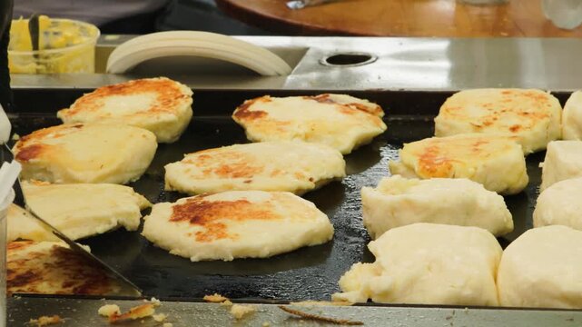 Cook hand flipping traditional Colombian Venezuelan cheese corn cakes arepas on flat griddle 60fps 4k